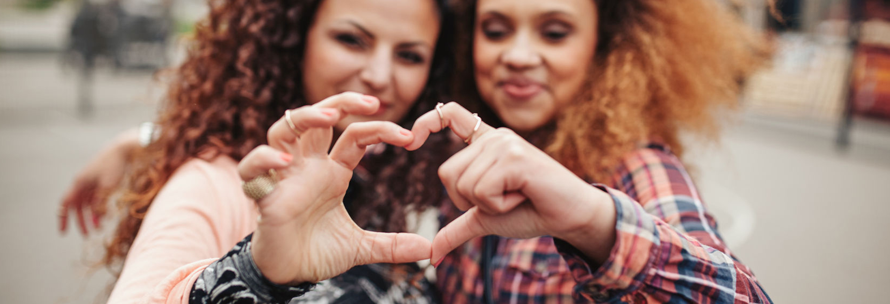 two black female each holding up an arm and creating a heart with fingers