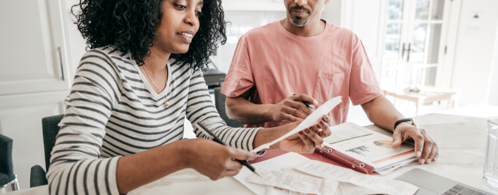 a black woman and a racially ambiguous man review their finances at a table together - financial education series New York Life Insurance Company